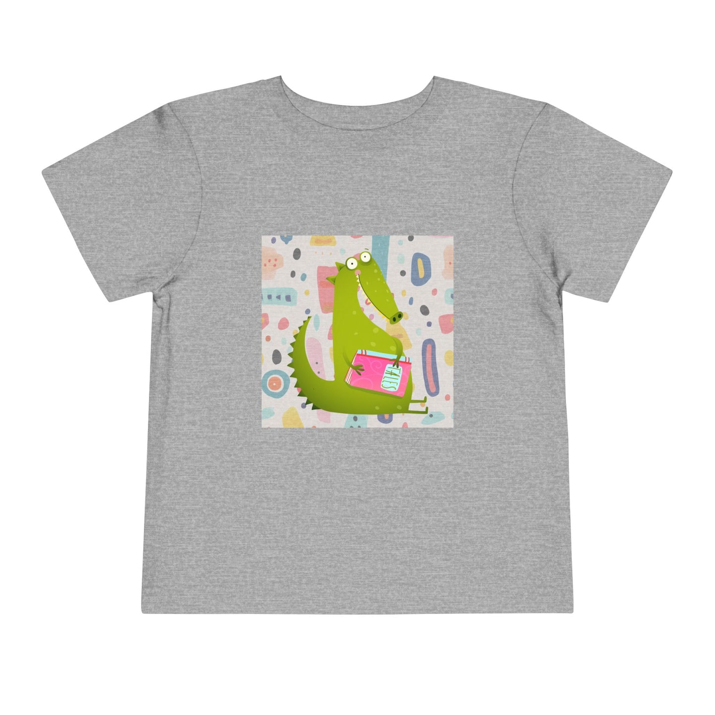Gray toddler t-shirt with a green gator, holding pink book and colorful pastel background