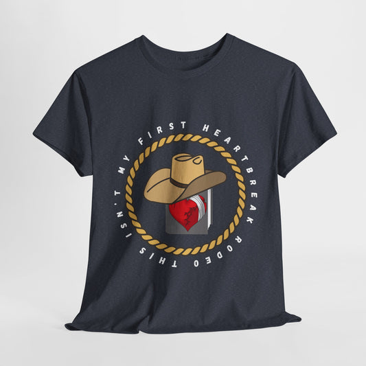 Gray t-shirt with a graphic design featuring a broken heart on the cover of a cowboy hat wearing book, encircled by rope and text 'This Isn't My First Heartbreak Rodeo'