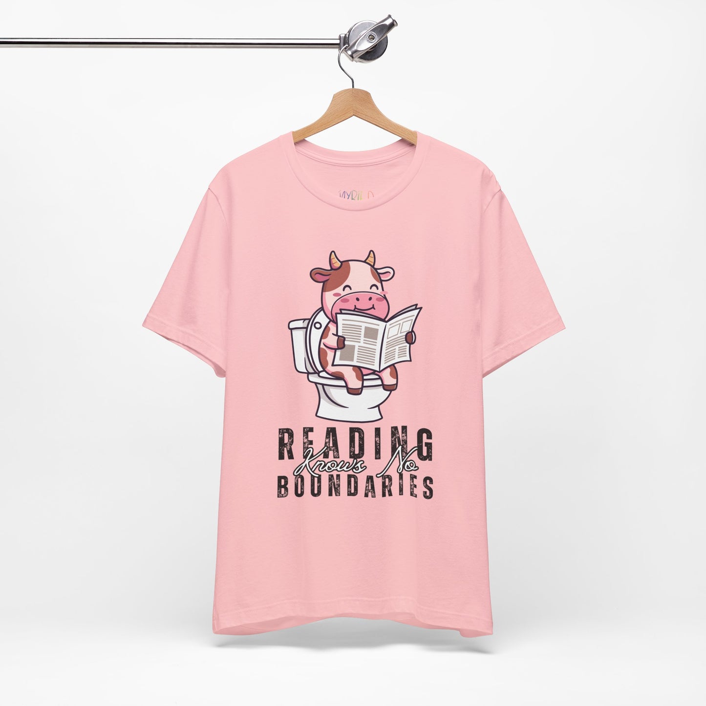 Pink t-shirt with a graphic of a cow on a toilet reading a newspaper, with text 'Reading Knows No Boundaries',