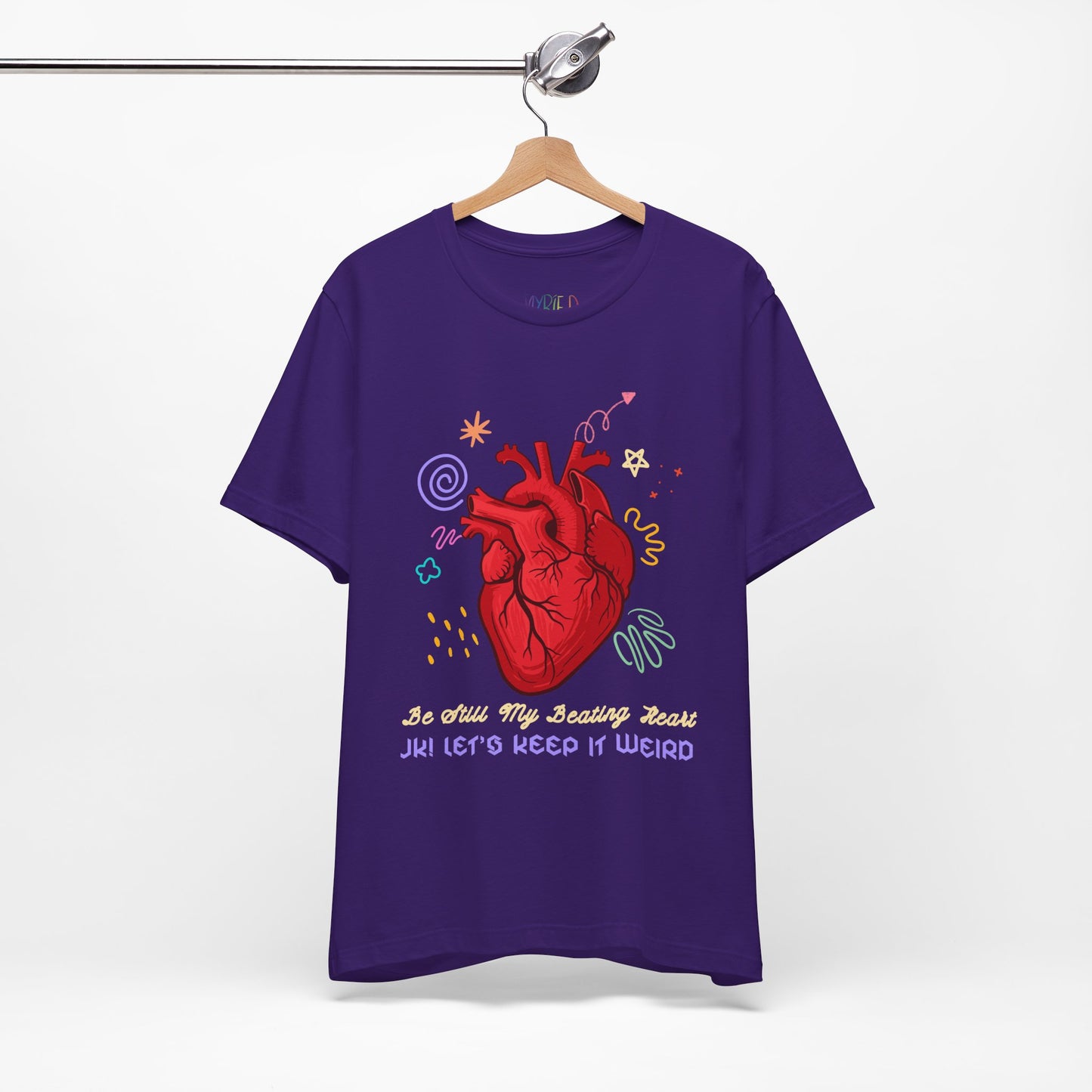 Purple t-shirt with a red anatomical heart surrounded by colorful doodles and text "Be Still My Beathing Heart. JK! Let's Keep It Weird'