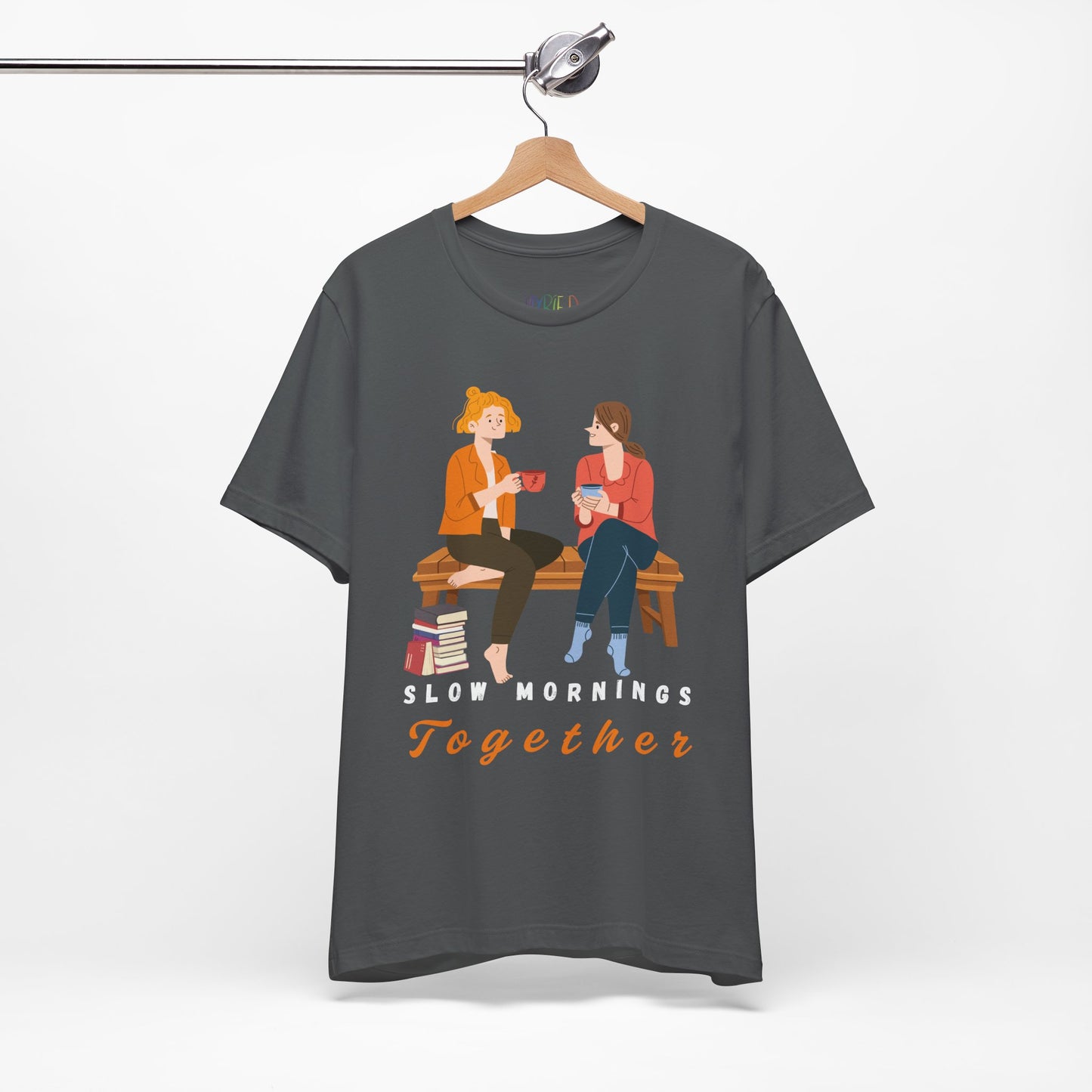 Gray t-shirt with graphic of two people sitting on a bench together, hot beverages in their hands, book at their feet and 'Slow Mornings Together' text below the image