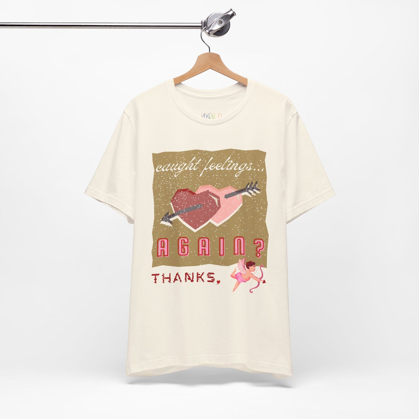 Beige t-shirt with double heart graphic design and text 'Caught Feelings AGAIN? Thanks,' followed by a picture of cupid