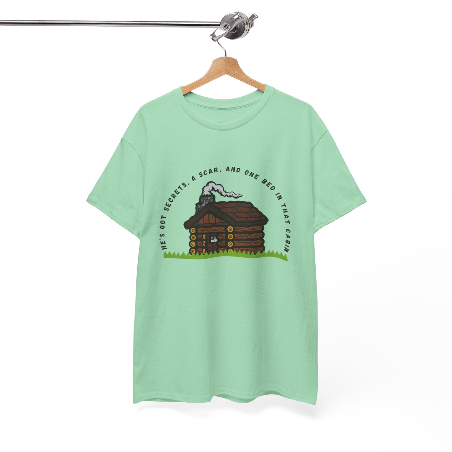 Light green t-shirt with cabin graphic and text 'He's Got Secrets, A Scar, And One Bed In That Cabin'