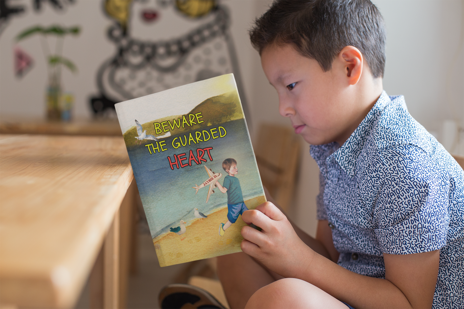 Boy sitting cross legged as he reads the children's picture book 'Beware The Guarded Heart' by Jaybie D.