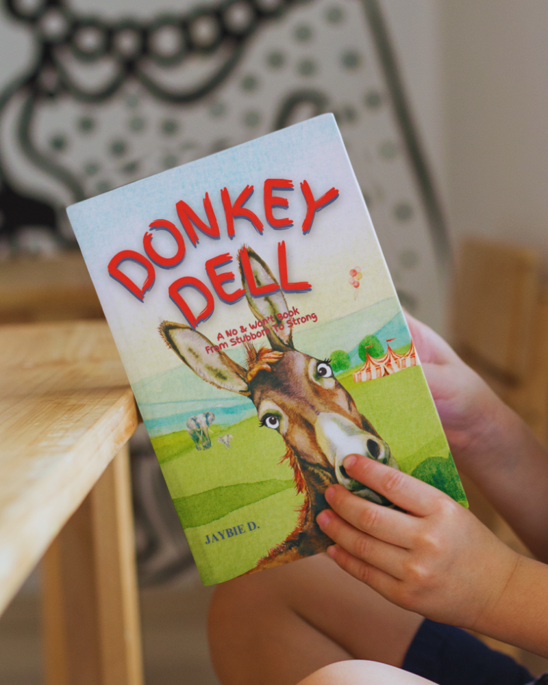Book titled 'Donkey Dell' by Jaybie D. held by a child with a blurred background