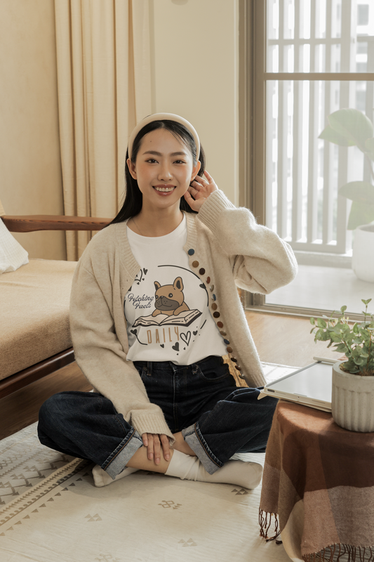 Woman sitting cross legged on the floor, wearing a beige and brown bookish t-shirt by Jaybie D.