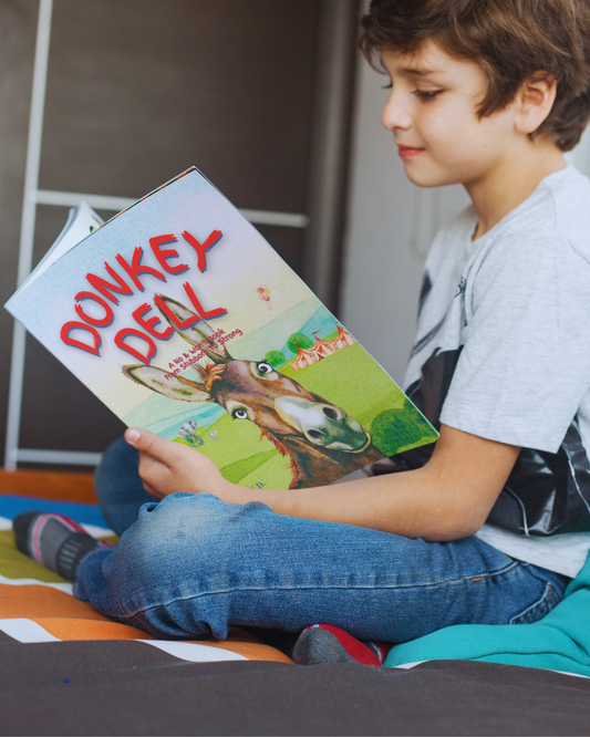 Boy sitting cross legged on his bed, reading picture book Donkey Dell by Jaybie D.