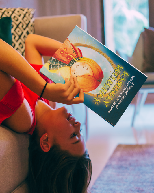 Young girl laying with her head hanging off the couch, as she reads children's picture book Rascally Reflection by Jaybie D.