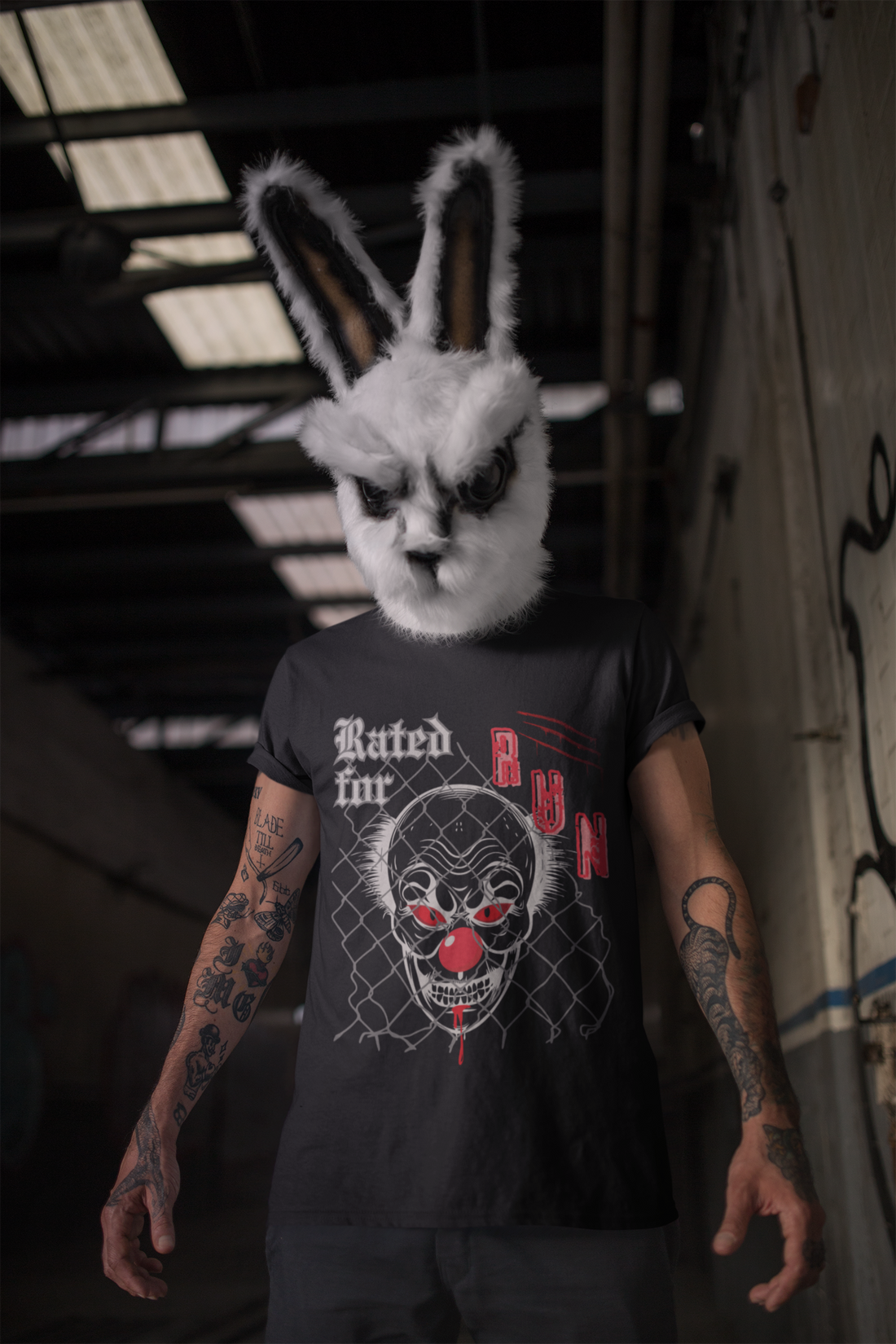 Image of a tattooed man is a dark hallway, wearing a scary bunny mask and a black t-shirt by Jaybie D. with an image of a clown and text 'Rated for RUN'