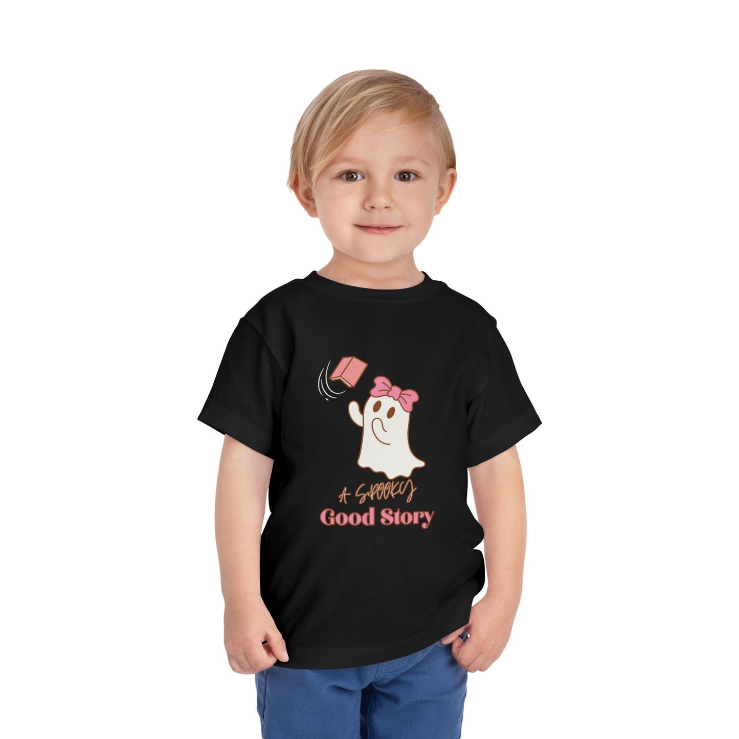 Child wearing a black toddler t-shirt with a ghost trying to catch a floating pink book with text 'A SPOOKY GOOD STORY'
