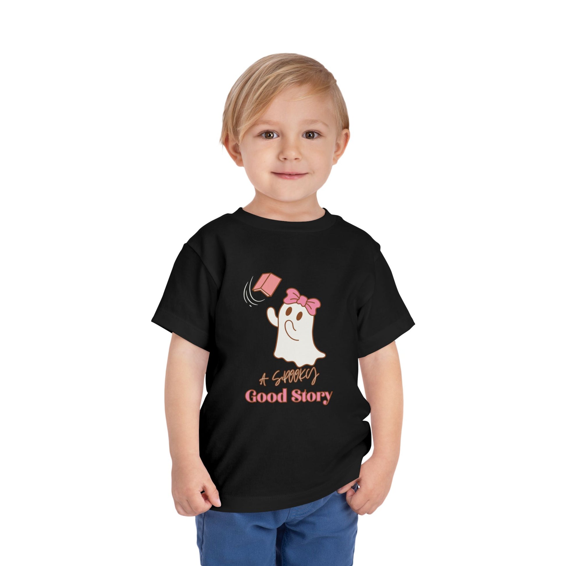 Child wearing a black toddler t-shirt with a ghost trying to catch a floating pink book with text 'A SPOOKY GOOD STORY'