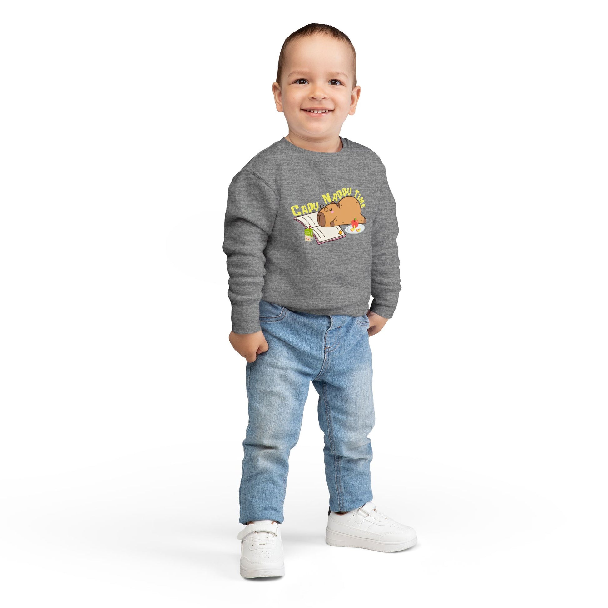 Boy wearing a gray toddler sweatshirt with a napping capybara, snacks, an open book and text 'Capo Nappy Time'