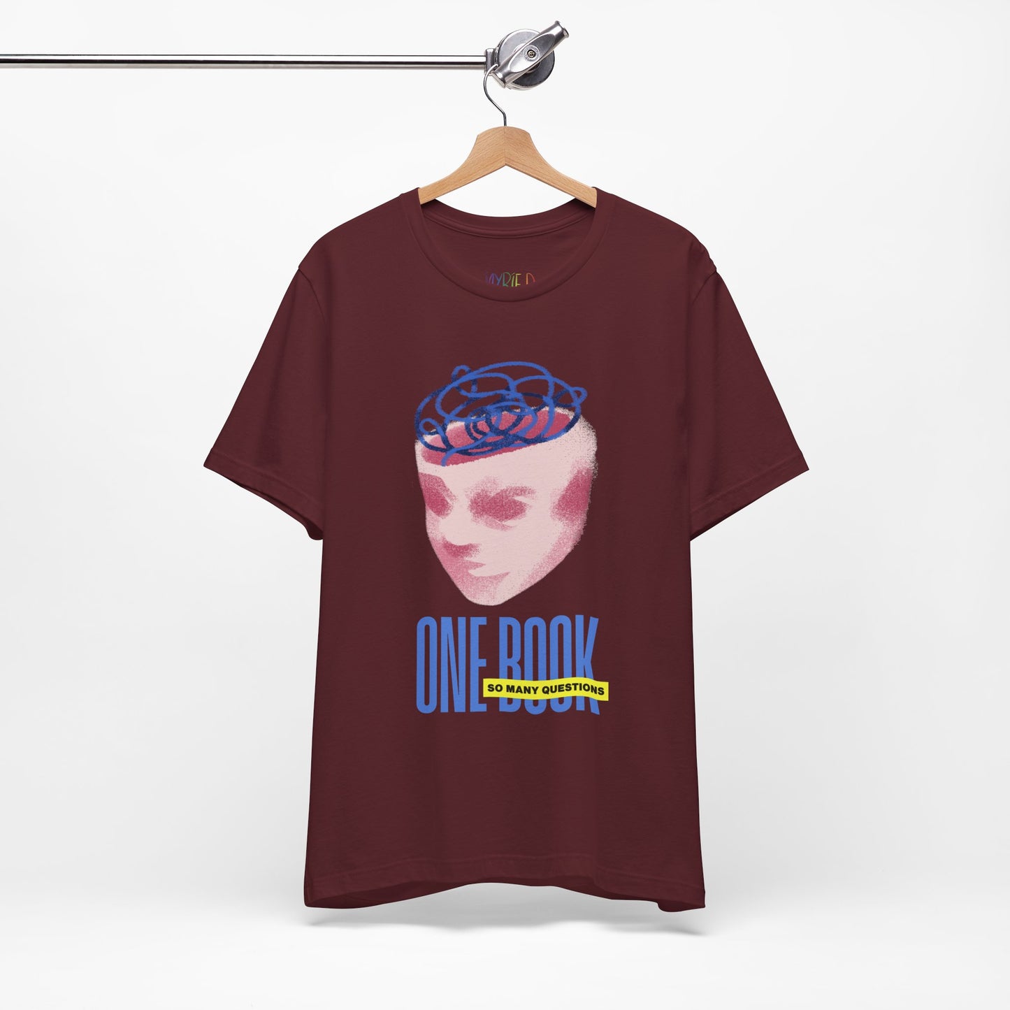 Maroon t-shirt with a pink face/head graphic, blue swirls coming out of the top and text 'One Book So Many Questions'