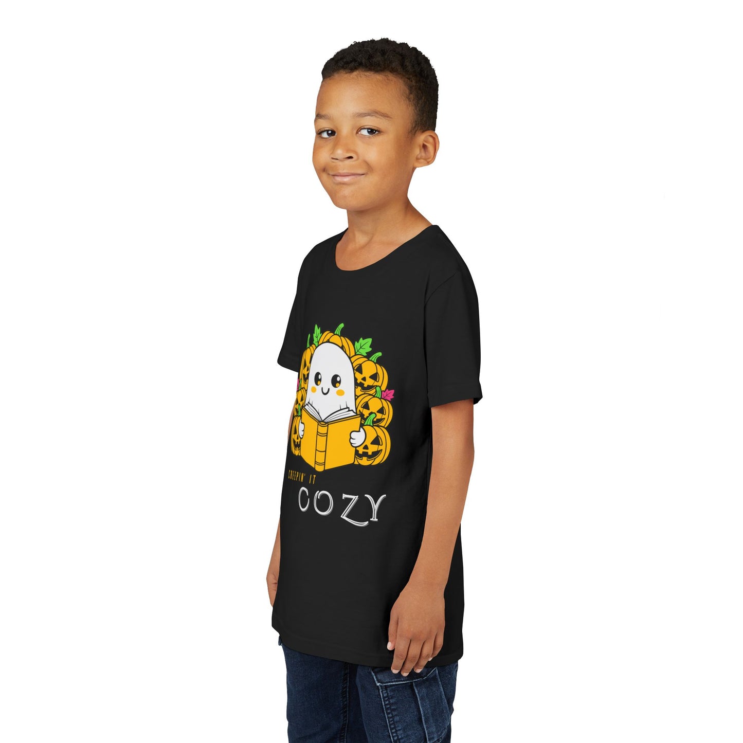 Boy wearing a black t-shirt with a ghost reading a book in a pumpkin patch with text 'Creepin' It Cozy'