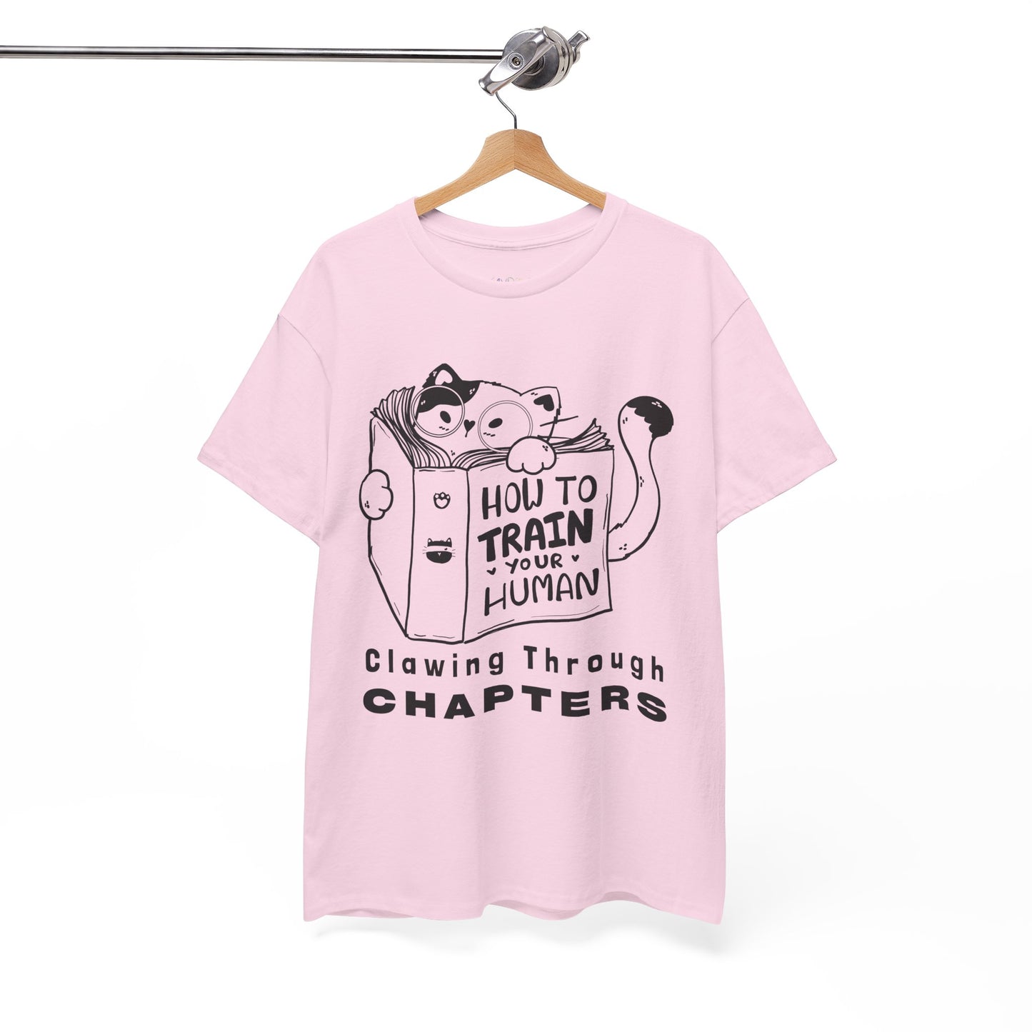 Pink t-shirt with black graphic design of a cat reading a 'How To Train Your Human' book and text 'Clawing Through Chapters'
