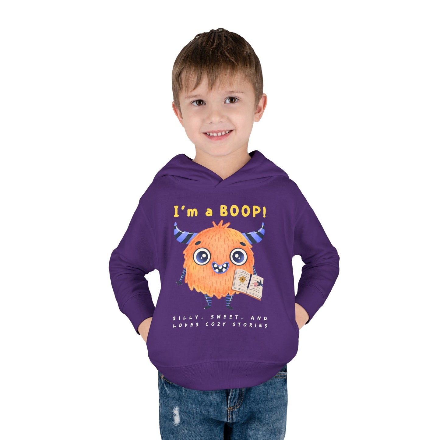 Boy wearing a purple toddler hoodie with a cartoon monster holding a book and text 'I'm a Boop', sub-text 'Silly, Sweet, And Loves Cozy Stories' on white background