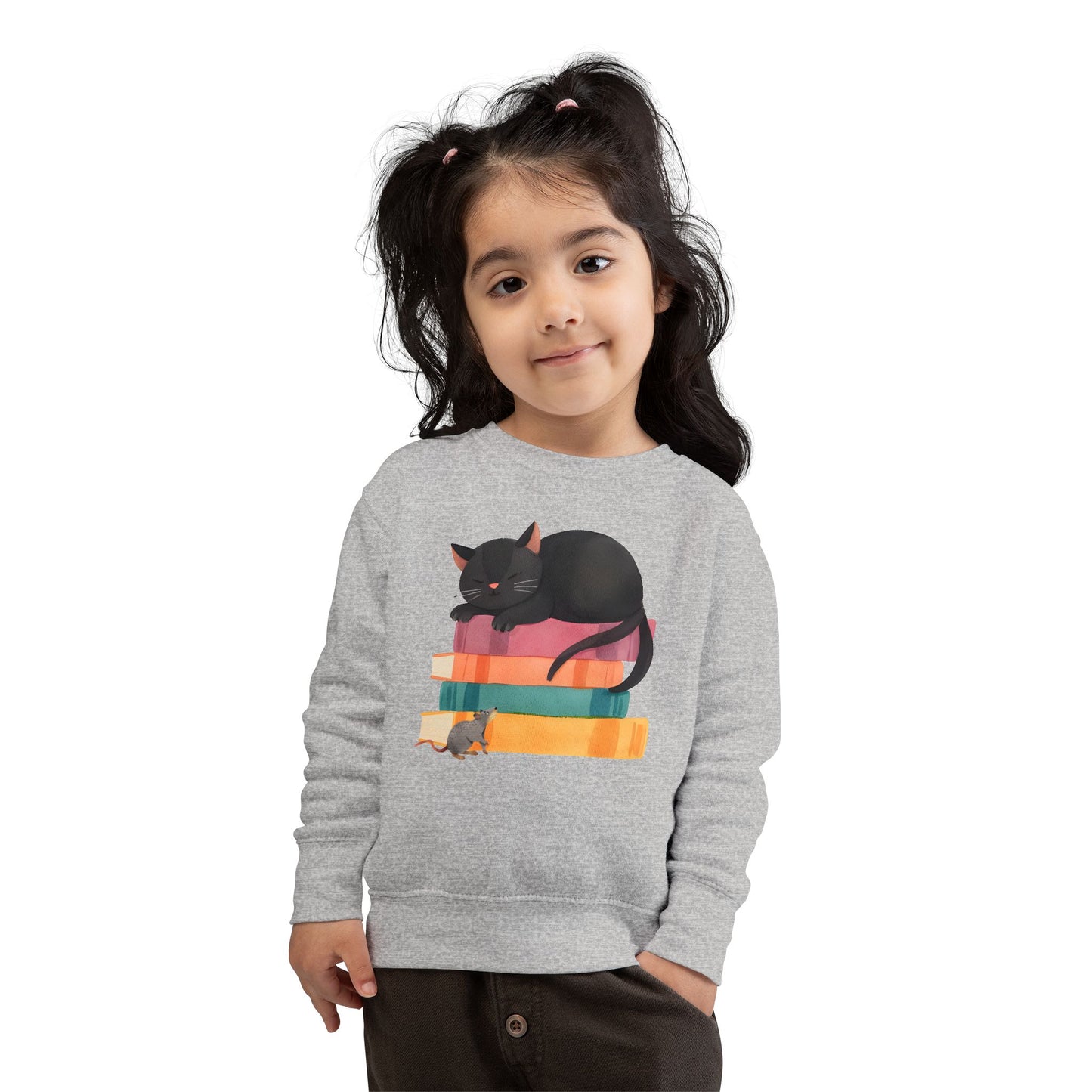 Girl wearing a gray toddler sweatshirt with a mouse looking up at a black cat sleeping on top of a stack of books 