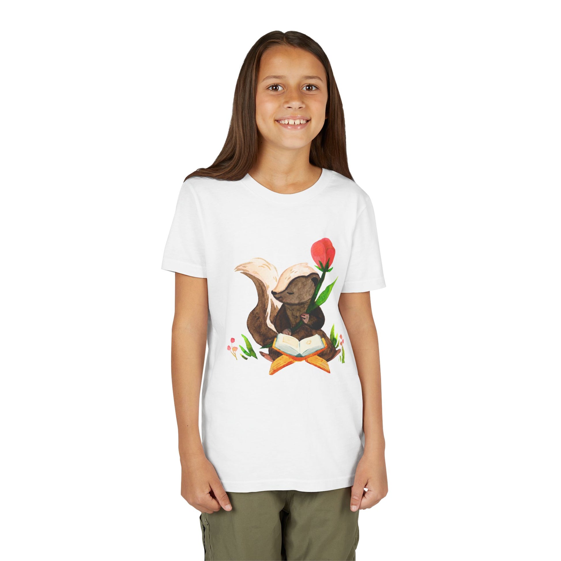Girl wearing a white t-shirt with a graphic of a skunk reading a book in a patch of flowers
