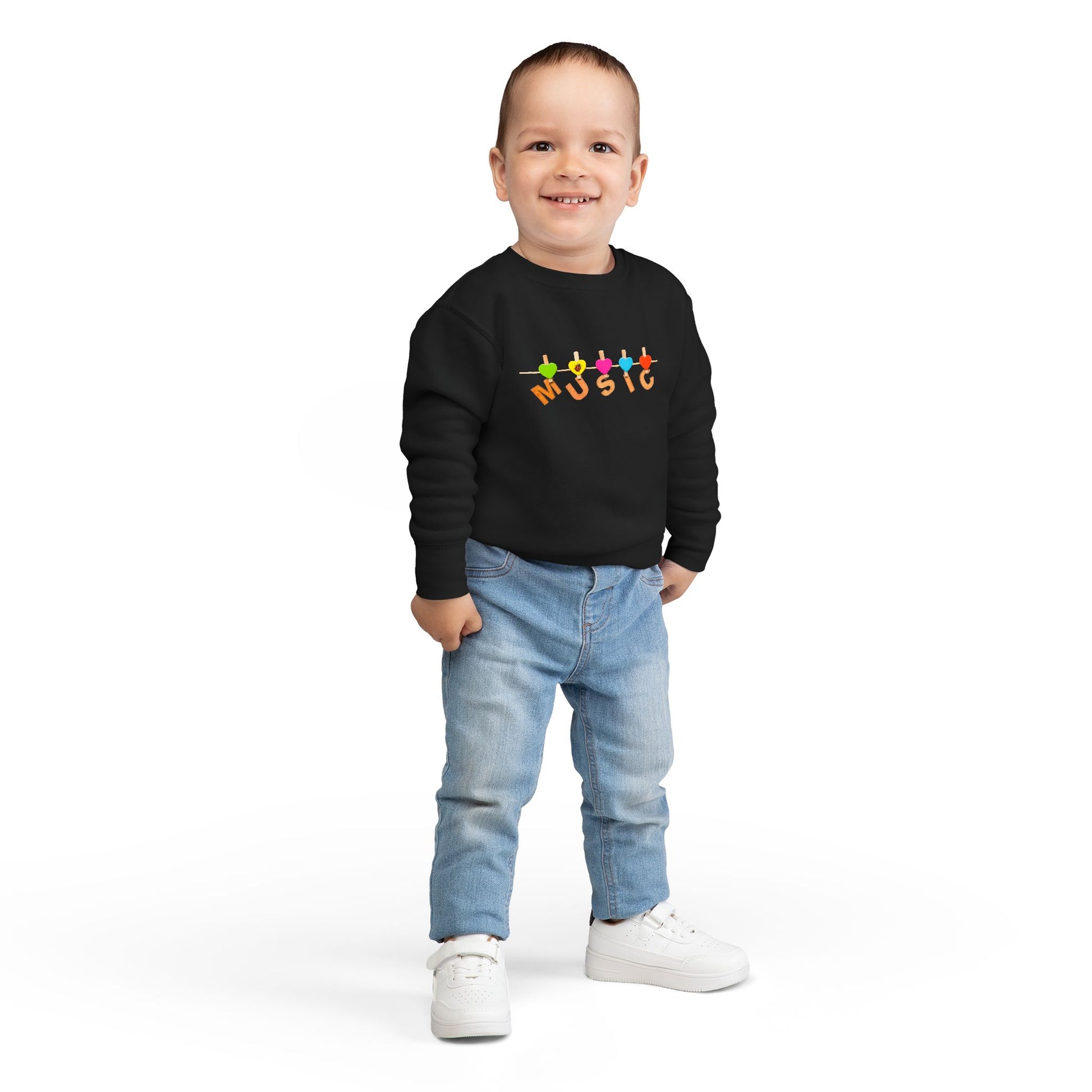 Boy wearing a black toddler sweatshirt with colorful letters hanging with clothespins to spell 'MUSIC'
