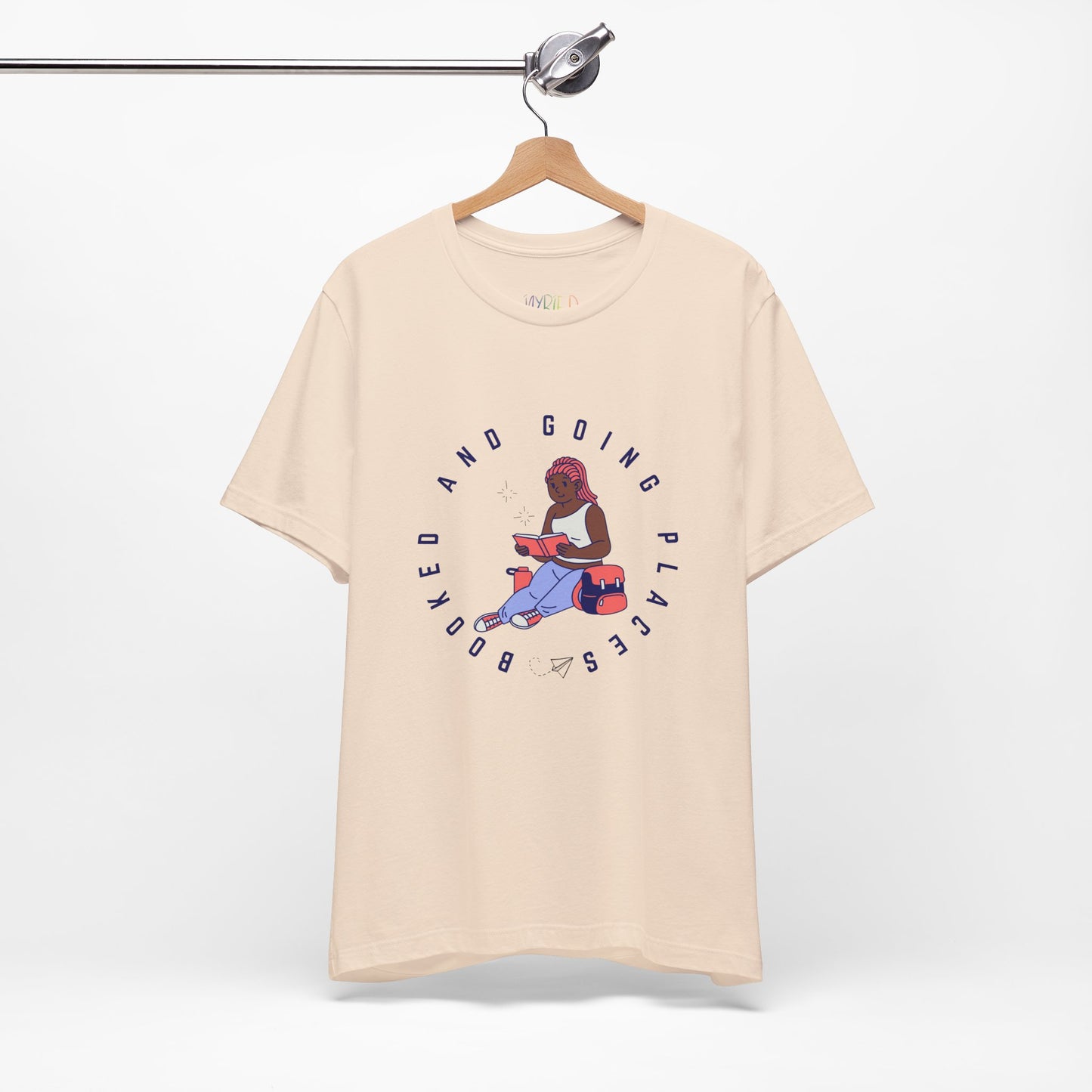 Beige t-shirt with graphic design of a school girl sitting with a book and text 'Booked And Going Places'