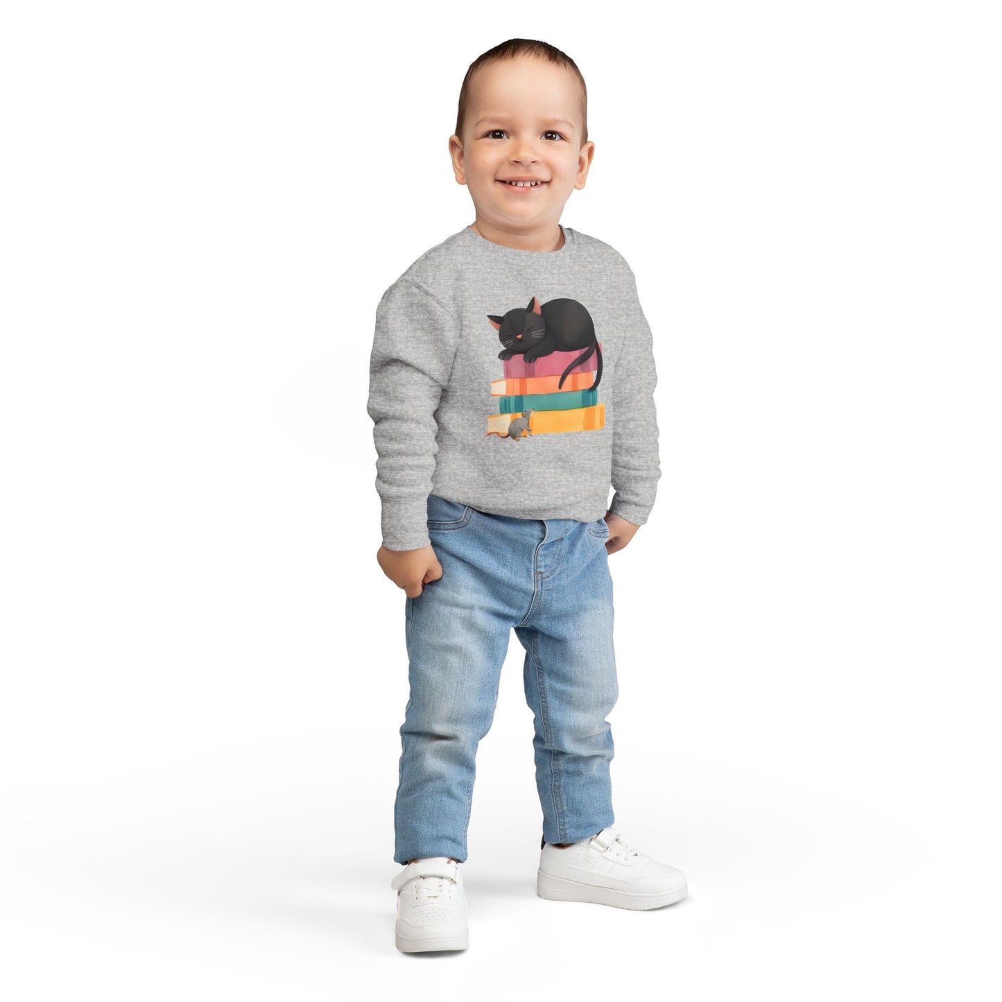 Boy wearing a gray toddler sweatshirt with a mouse looking up at a black cat sleeping on top of a stack of books 