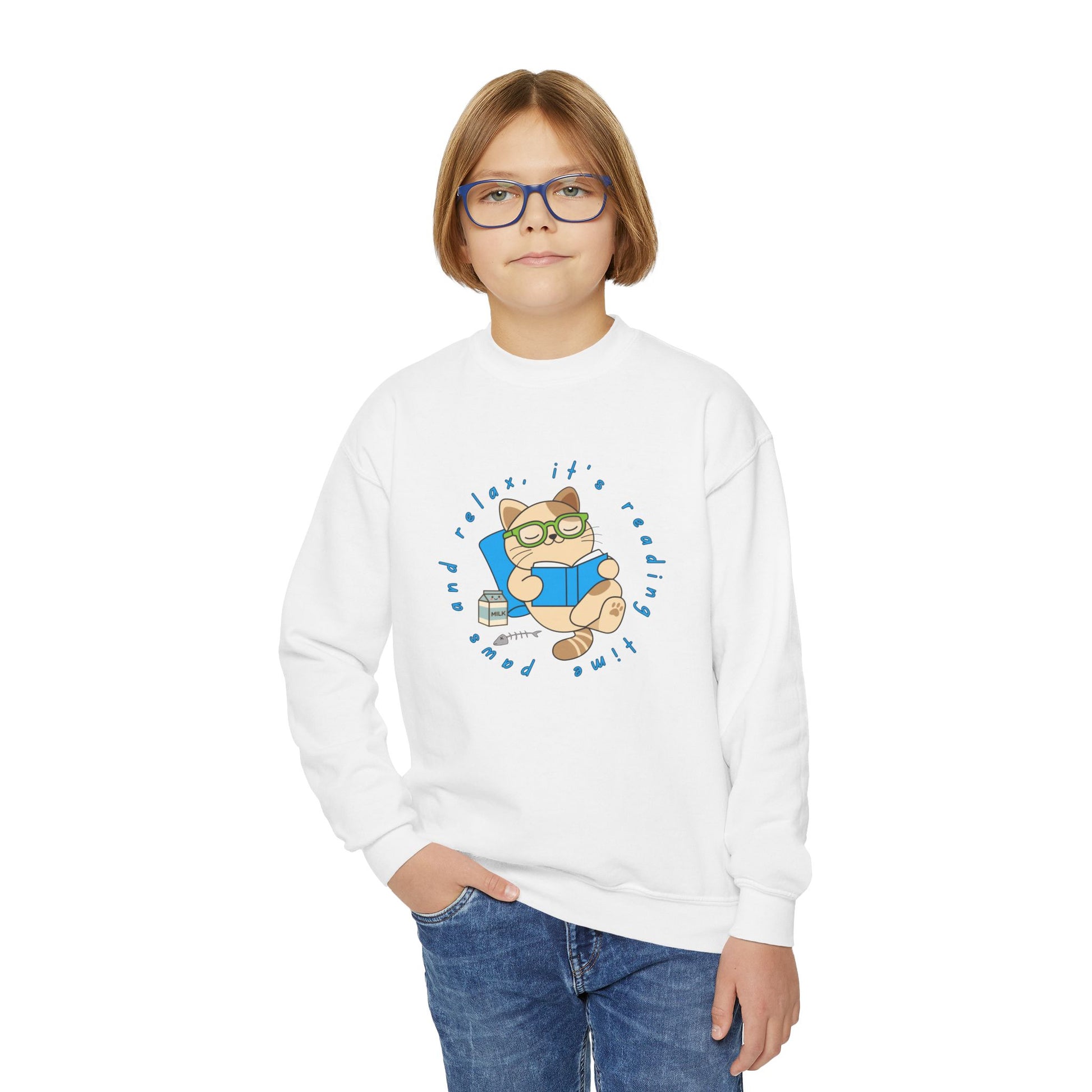 Boy wearing a white sweatshirt with a cartoon cat reading a book, circled by text 'paws and relax, it's reading time'