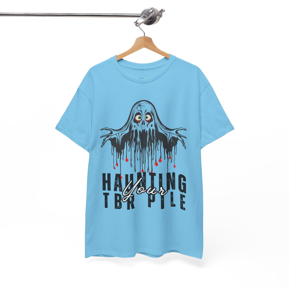 A light blue short-sleeve t-shirt hanging on a wooden hanger from a metal rack. The shirt features a graphic of a dripping black ghost with red blood-like drips and the text 'HAUNTING YOUR TBR PILE' printed below it.