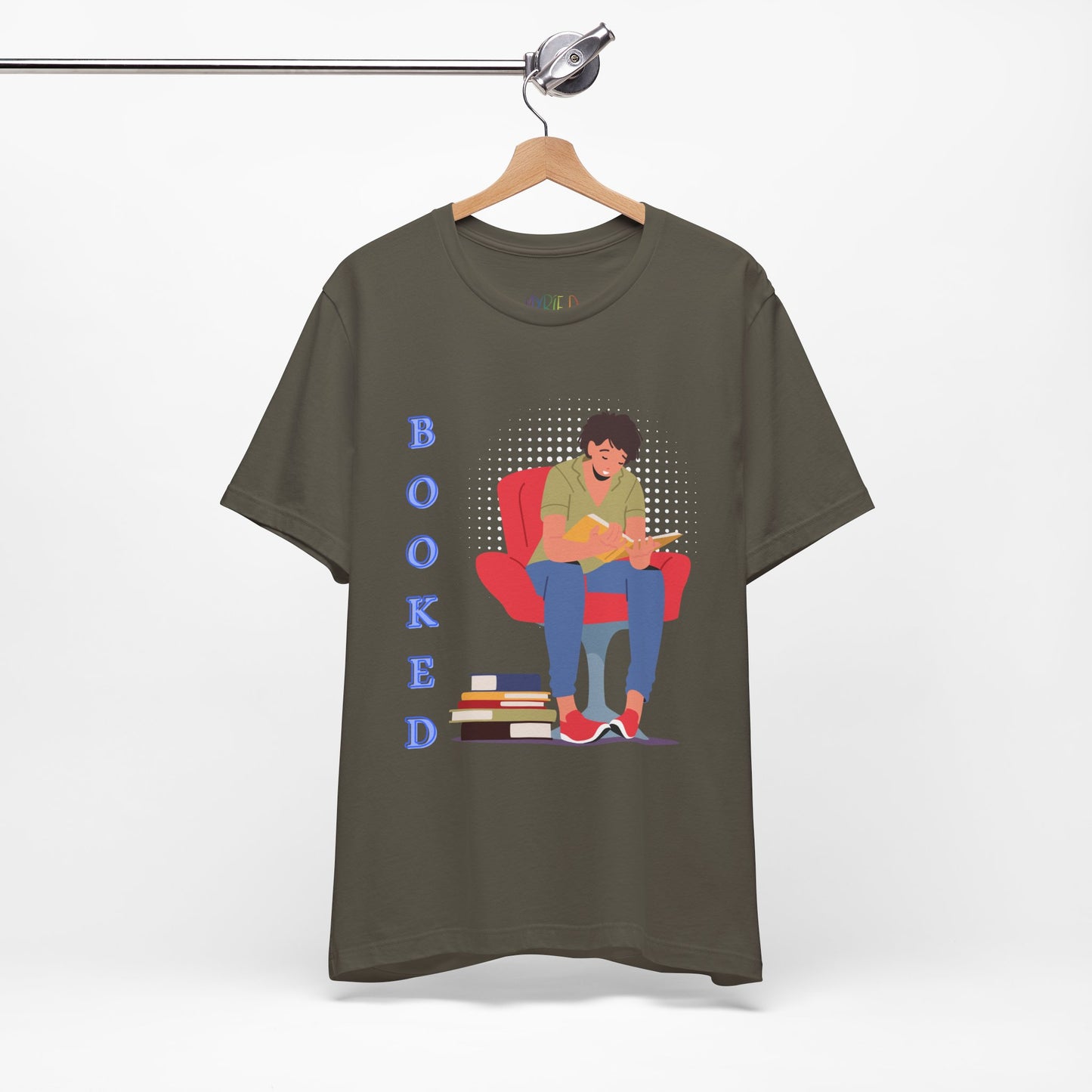 Army green t-shirt with a graphic of a person sitting in a chair, reading a book, a stack of books at his feet and text 'BOOKED' 