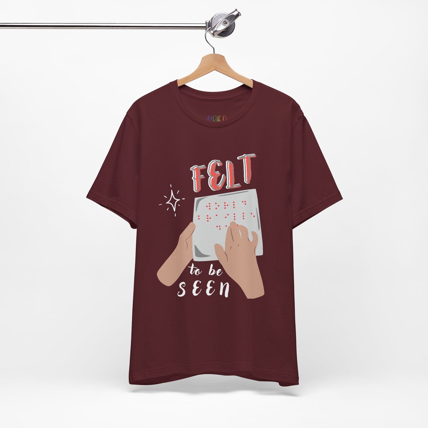 Maroon t-shirt with graphic design of hands reading braille text and 'Felt To Be Seen' messaging 