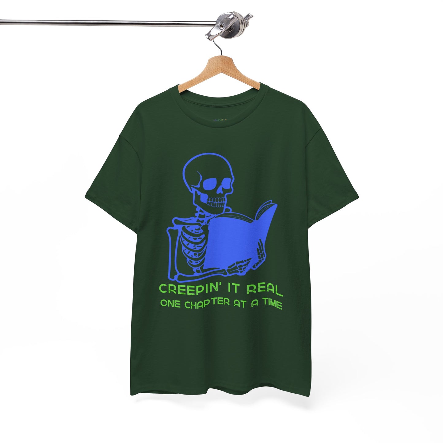 Green t-shirt with blue skeleton graphic reading a book and green text 'Creepin' It Real One Chapter At A Time' on a hanger against a white background