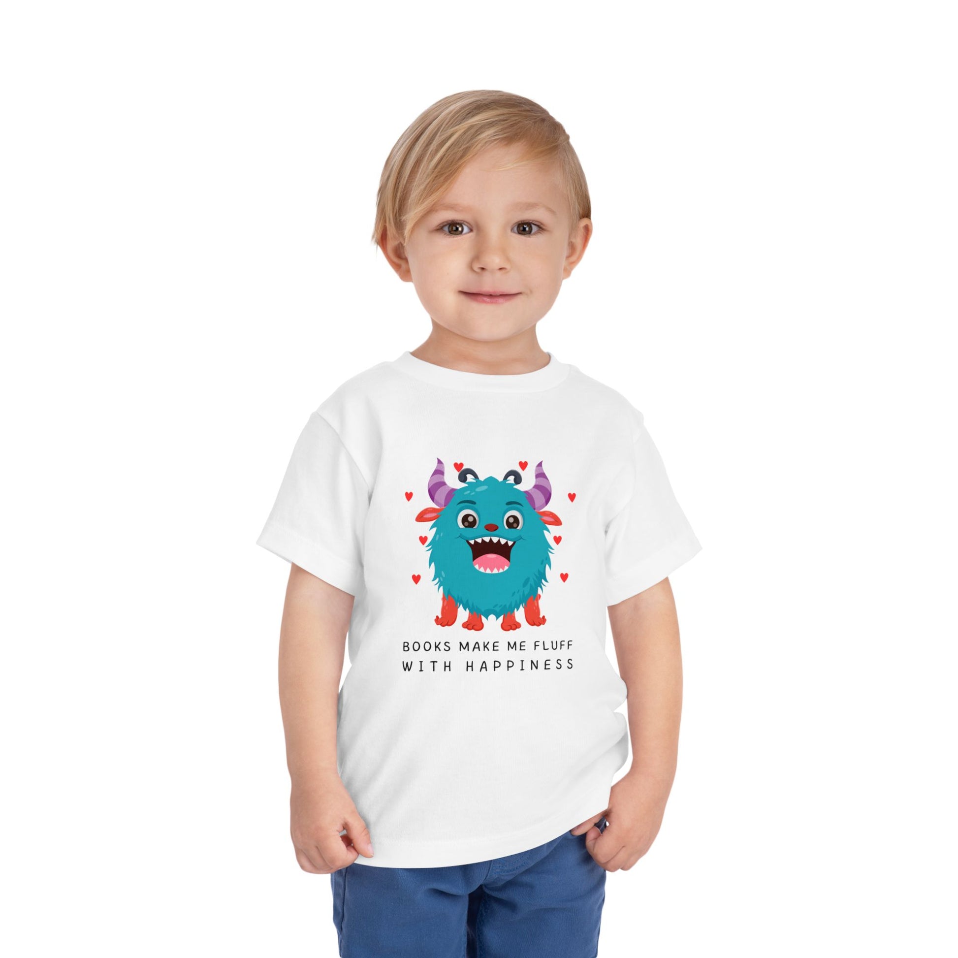Child wearing a white toddler t-shirt with a fluffy blue monster graphic, floating hearts and text 'Books Make Me Fluff With Happiness' on a white background
