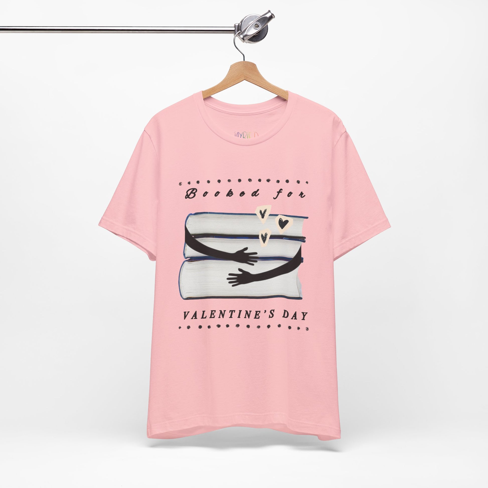 Pink t-shirt with a graphic design featuring arms hugging a stack of books and text 'Booked for Valentine's Day' 