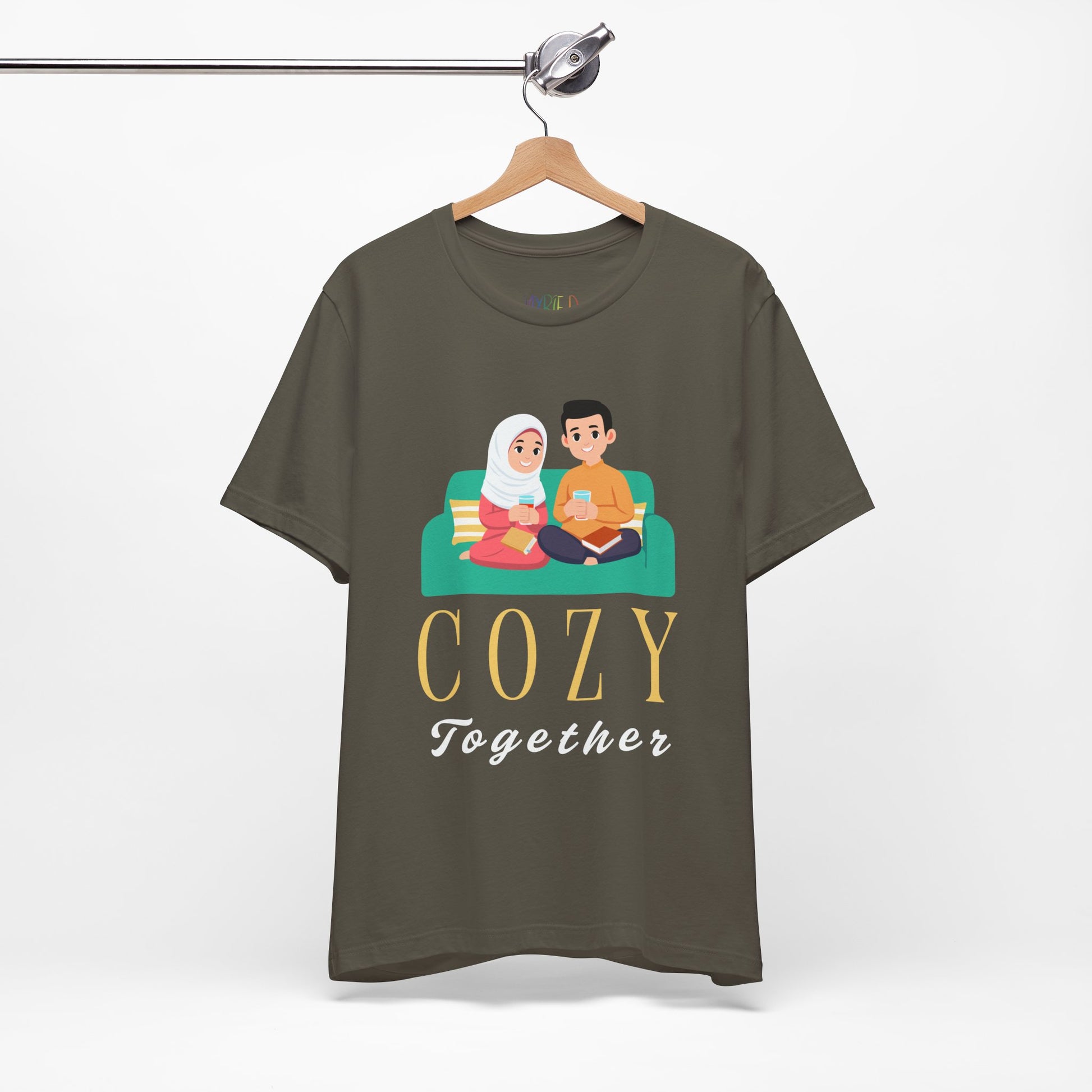 Green t-shirt with a graphic of two people on a couch, with books and drinks, the text 'Cozy Together' sits beneath in large letters