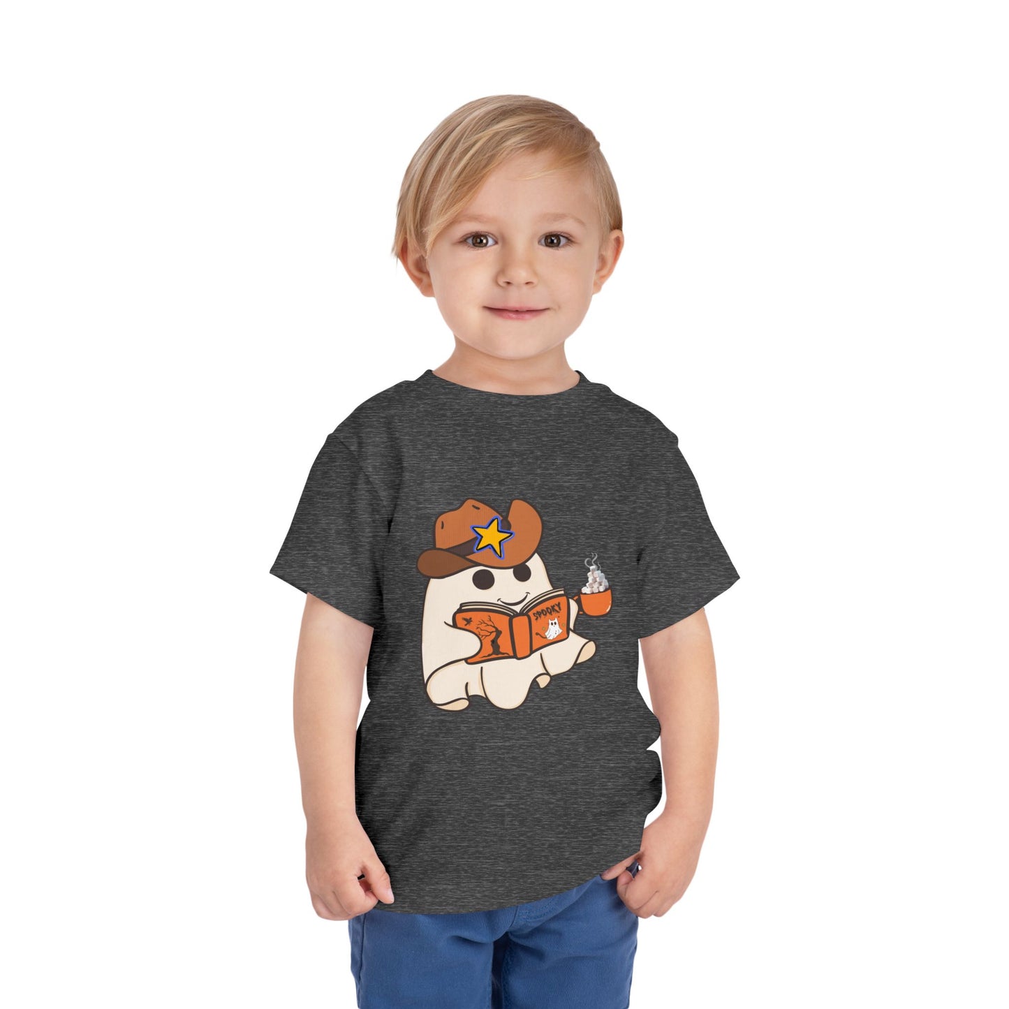Child wearing a gray toddler t-shirt with a cartoon ghost, wearing a cowboy hat, reading a spooky book and holding a cup of hot cocoa