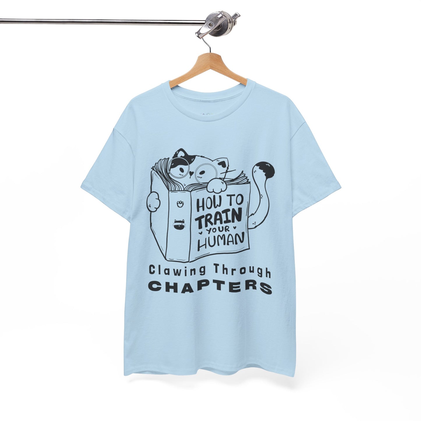 Light blue t-shirt with black graphic design of a cat reading a 'How To Train Your Human' book and text 'Clawing Through Chapters'