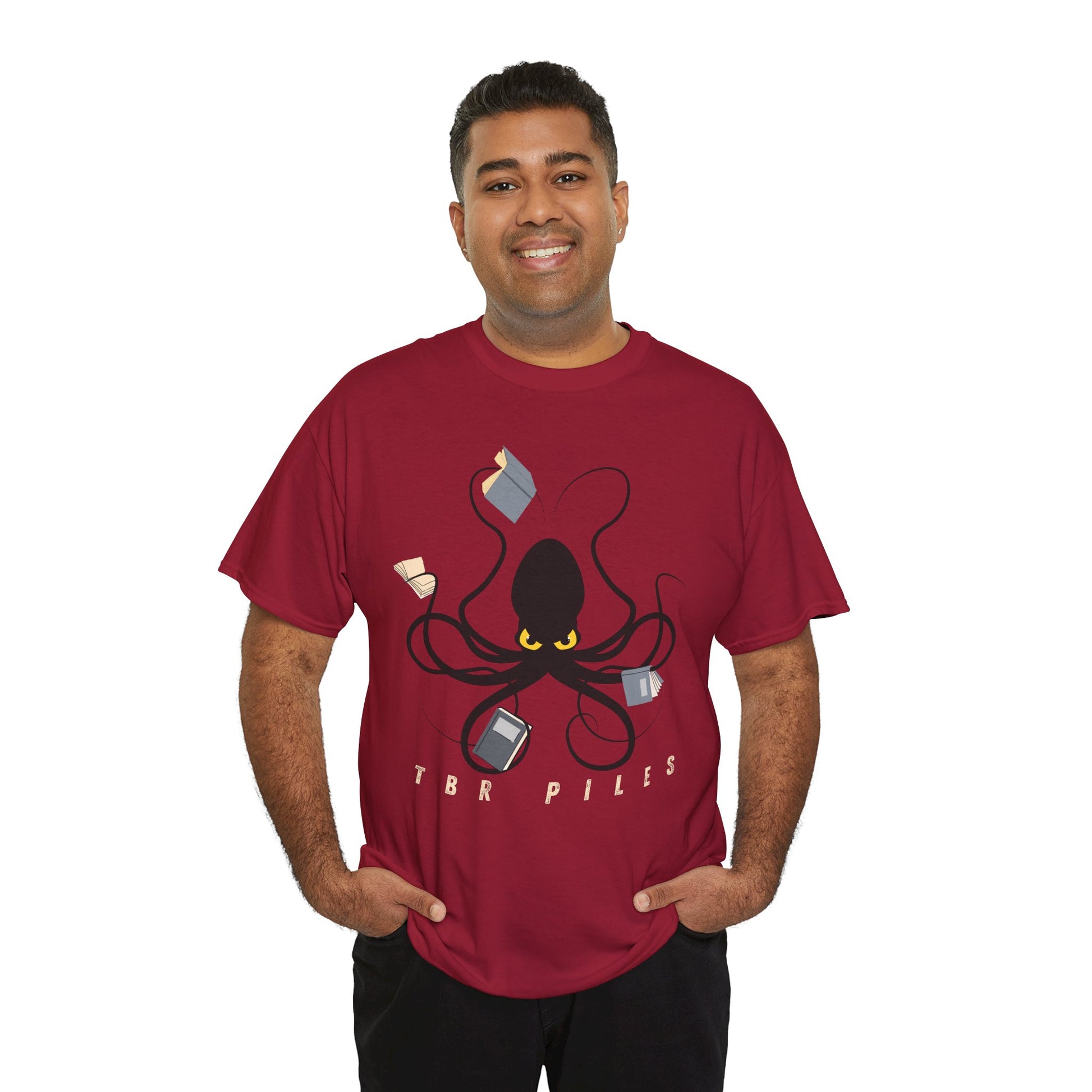 Man wearing a red t-shirt with a yellow eyed black octopus  holding several books and text 'TBR PILES' 