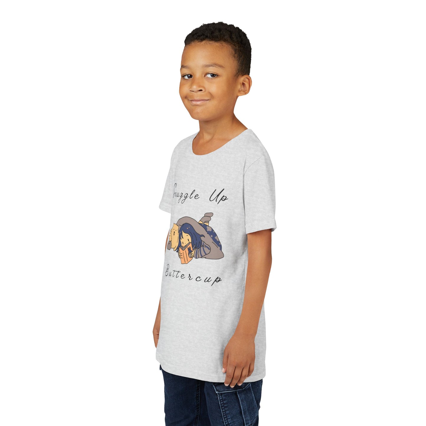 Boy wearing a light gray t-shirt with cartoon design of a girl and her dog reading a book under a blanket and text 'Snuggle Up Buttercup' 