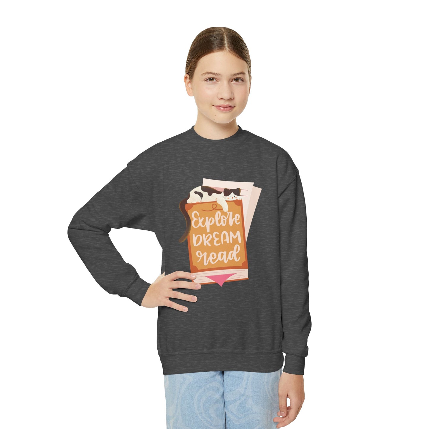 Girl wearing a dark gray sweatshirt with a graphic design of a cat sleeping on a book and text 'Explore. Dream. Read.'