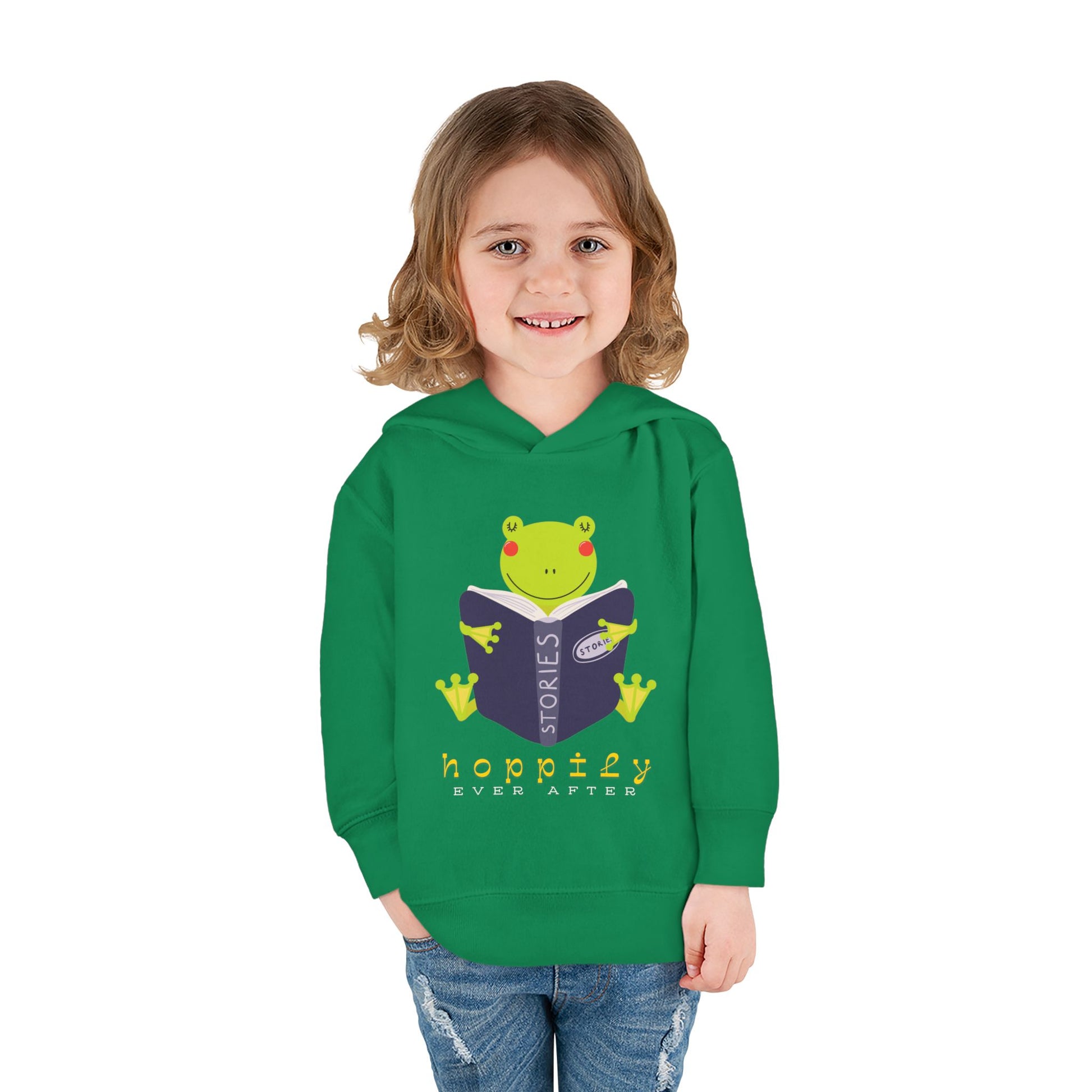 Girl wearing a green toddler hoodie with a frog hugging an open book and text 'hoppily ever after'