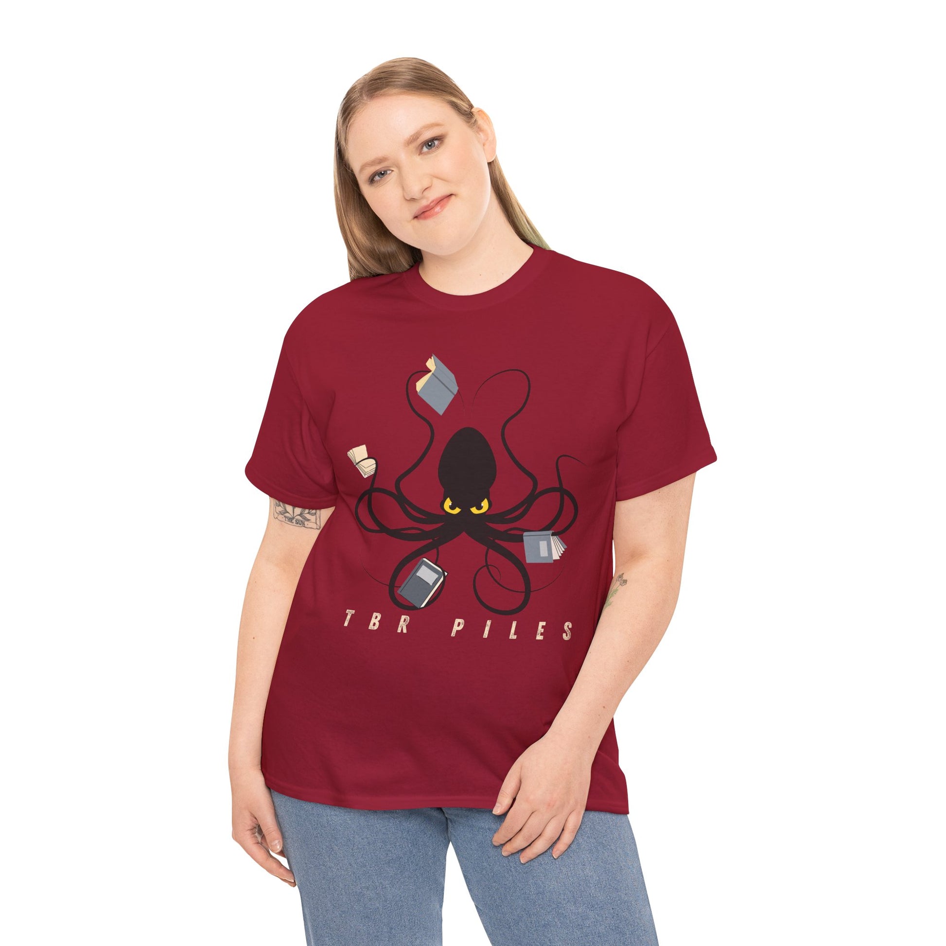 Woman wearing a red t-shirt with a yellow eyed black octopus  holding several books and text 'TBR PILES' 