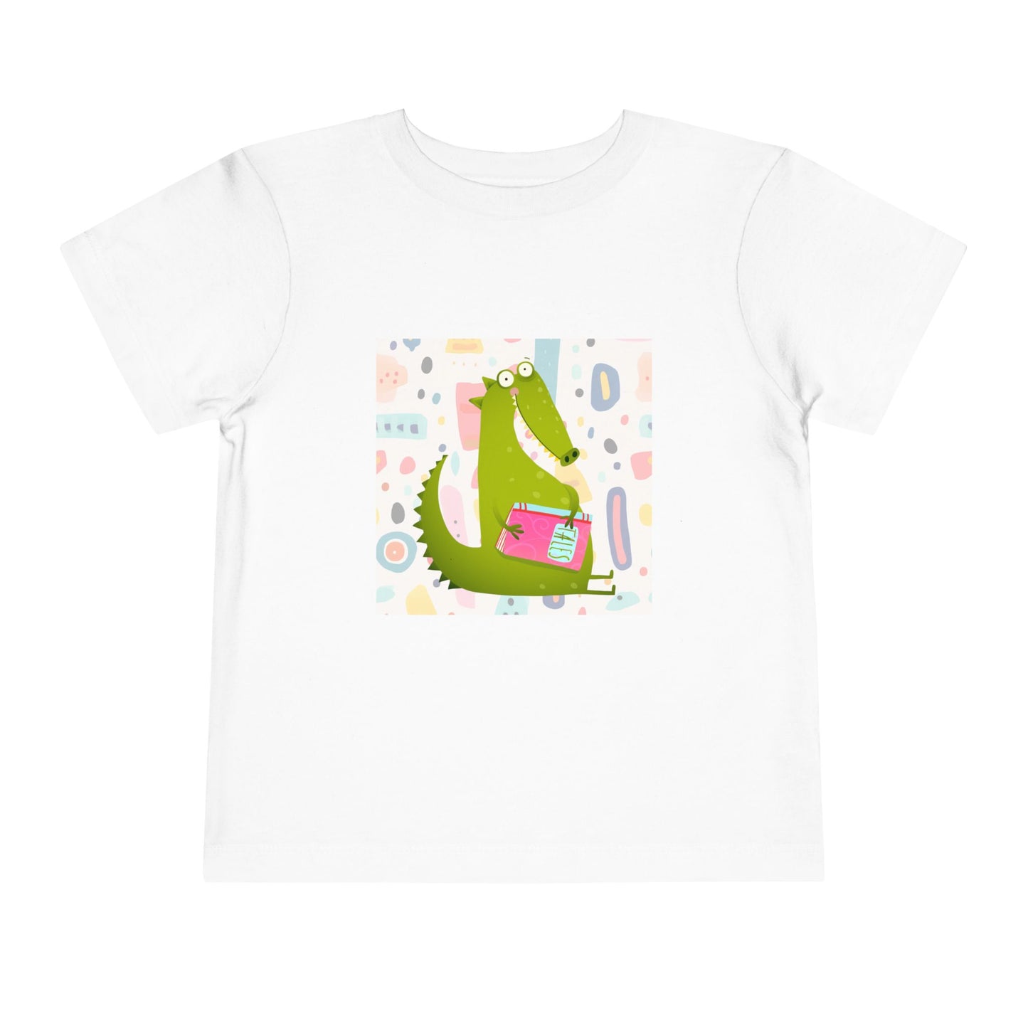 White toddler t-shirt with a green gator, holding pink book and colorful pastel background 