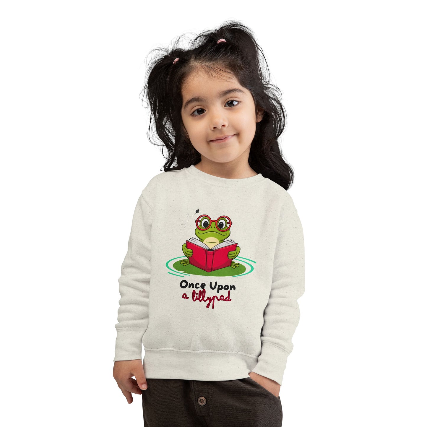 Girl wearing a beige toddler sweatshirt with a frog reading a book on a lillypad and text 'Once Upon a Lillypad' 