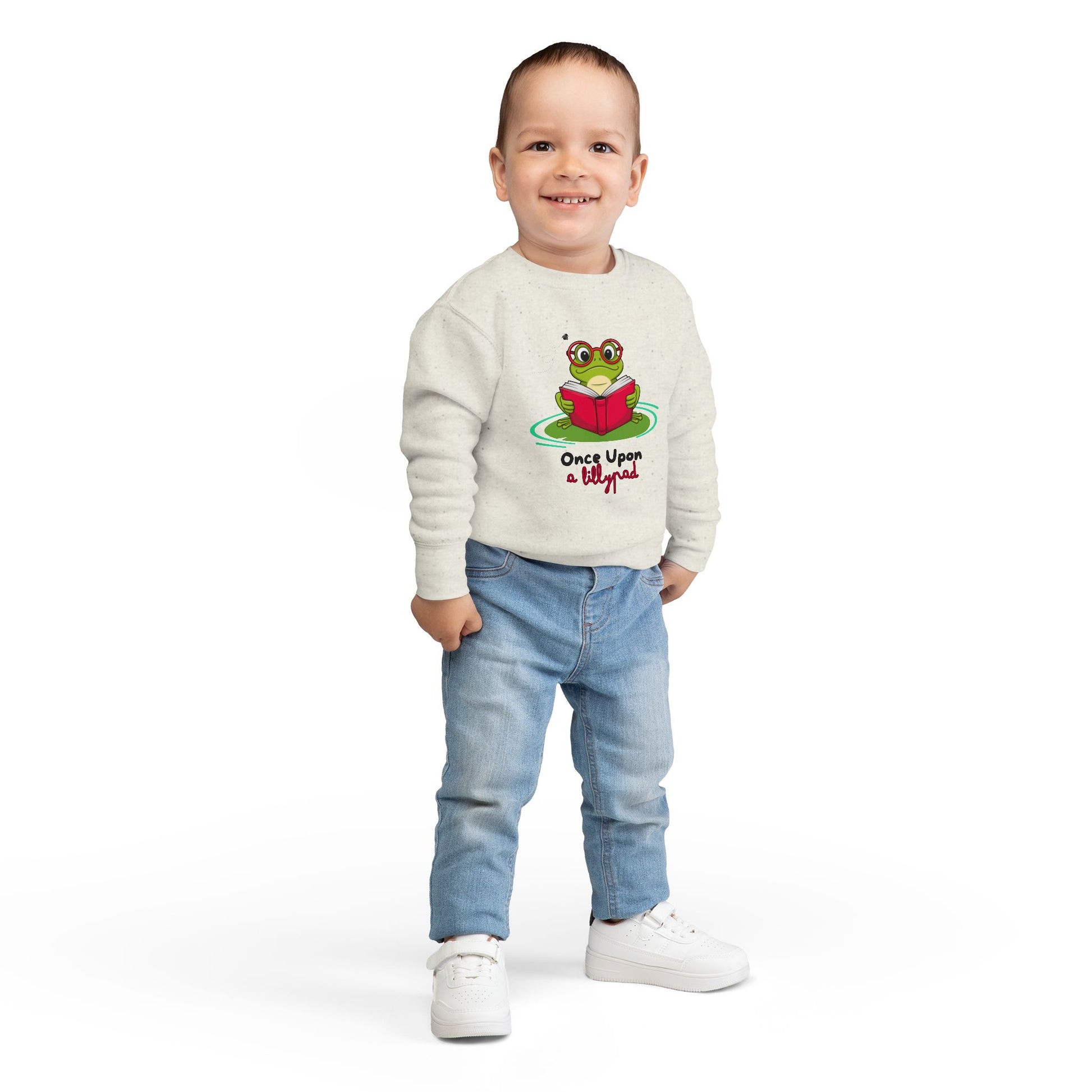 Boy wearing a beige toddler sweatshirt with a frog reading a book on a lillypad and text 'Once Upon a Lillypad' 