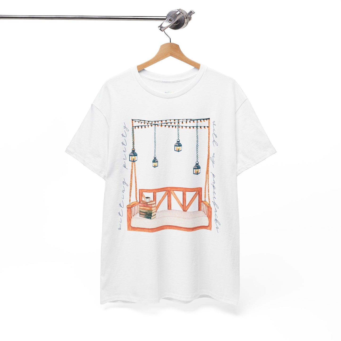 White t-shirt with a porch swing, string lights, hot beverage and a stack of books, text says 'Sitting Pretty With My Paperbacks'