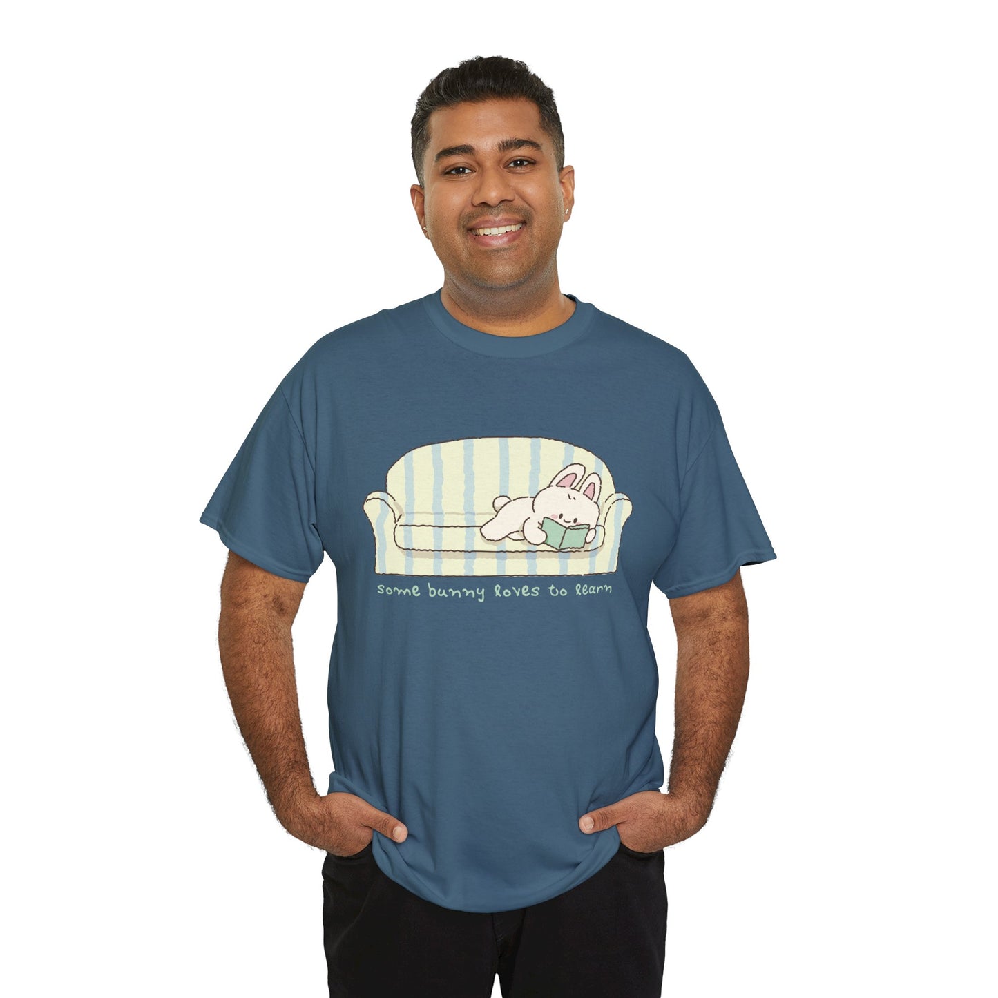 Man wearing a blue t-shirt with a cartoon bunny reading a book as it's lays on a couch, text 'some bunny loves to learn' 