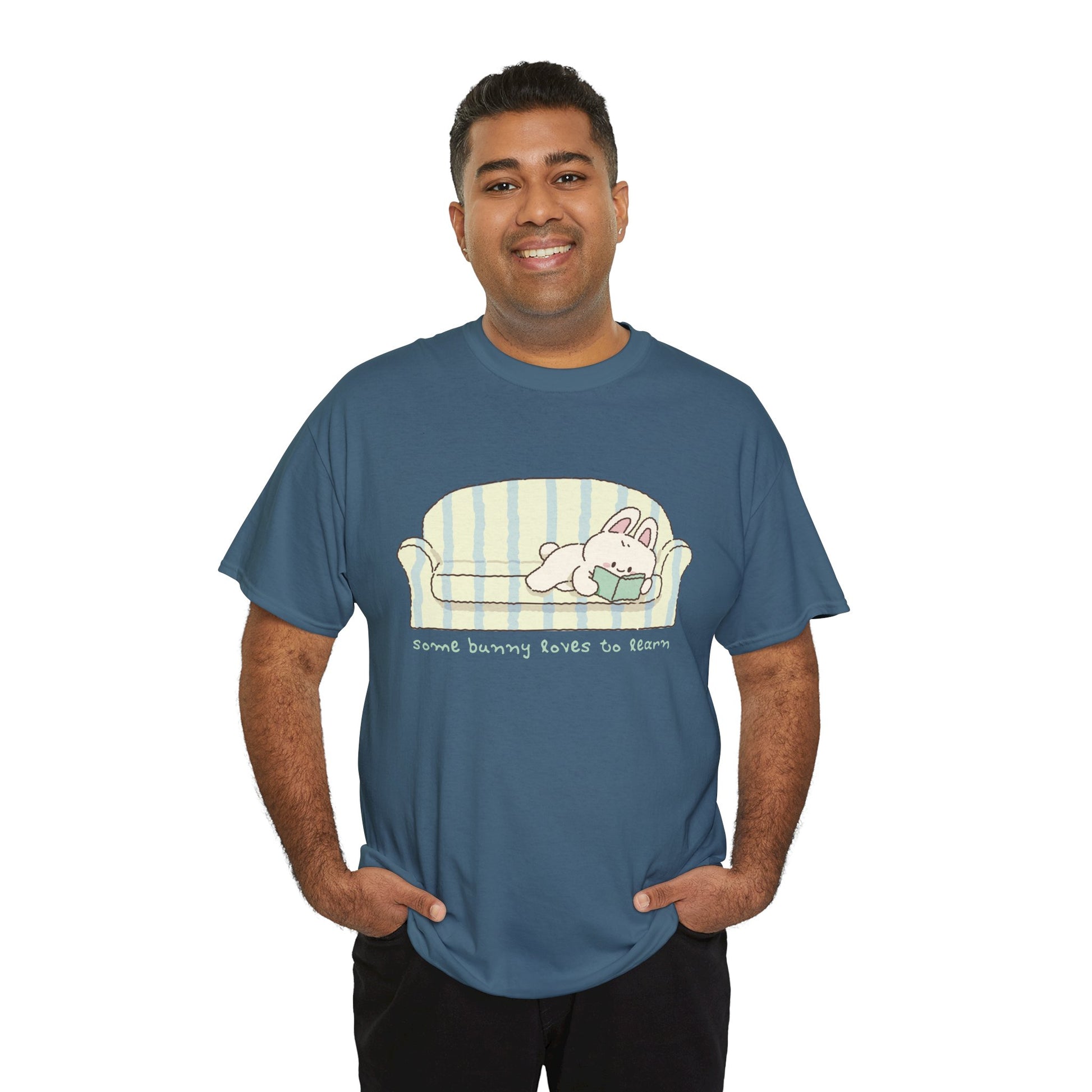 Man wearing a blue t-shirt with a cartoon bunny reading a book as it's lays on a couch, text 'some bunny loves to learn' 