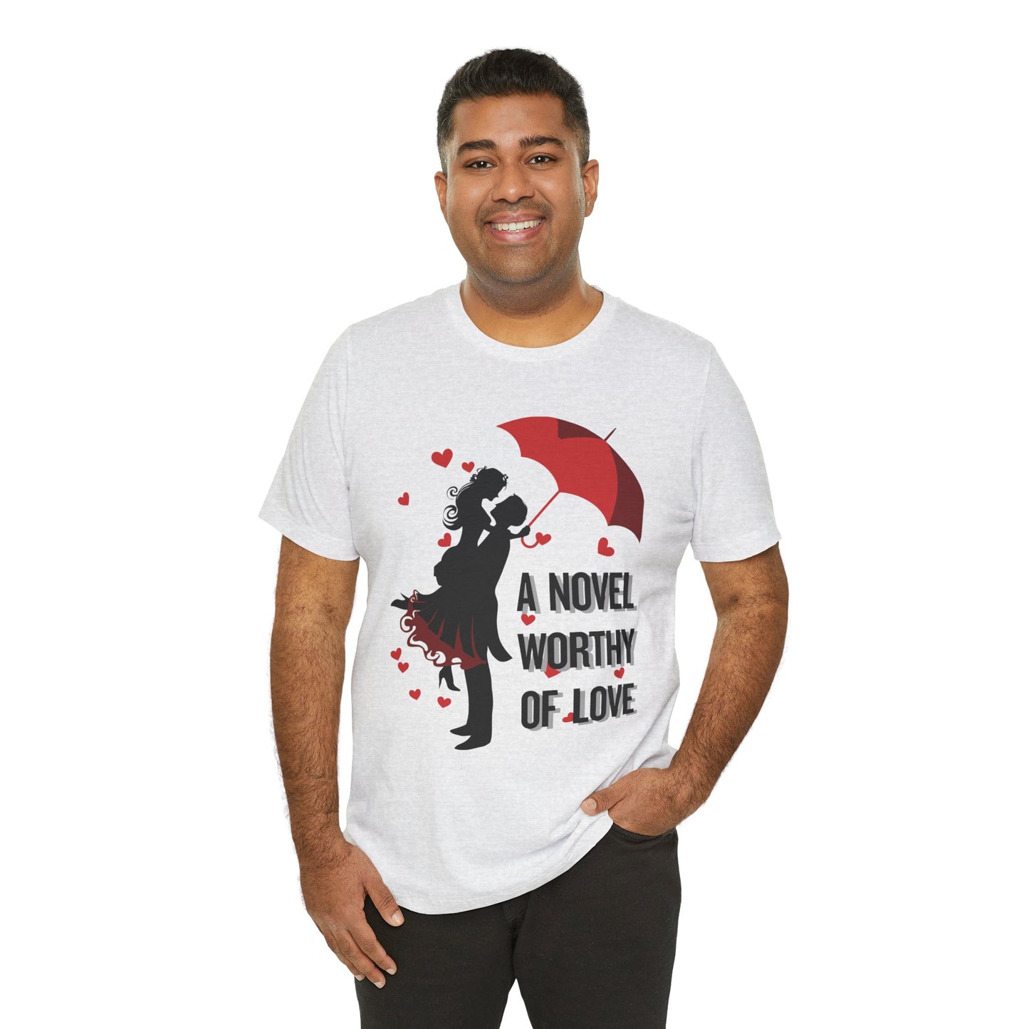 A man wearing an ash t-shirt with a black graphic design of a man holding a woman under a red umbrella, sprinkled with hearts and text 'A Novel Worthy of Love' 