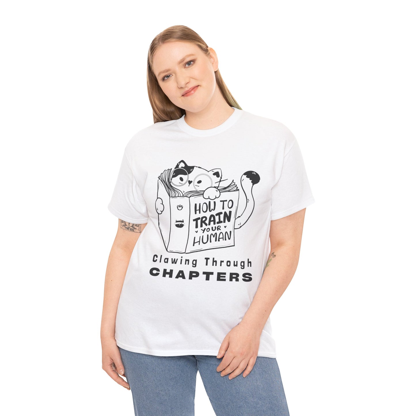 Woman wearing a white t-shirt with black graphic design of a cat reading a 'How To Train Your Human' book and text 'Clawing Through Chapters'