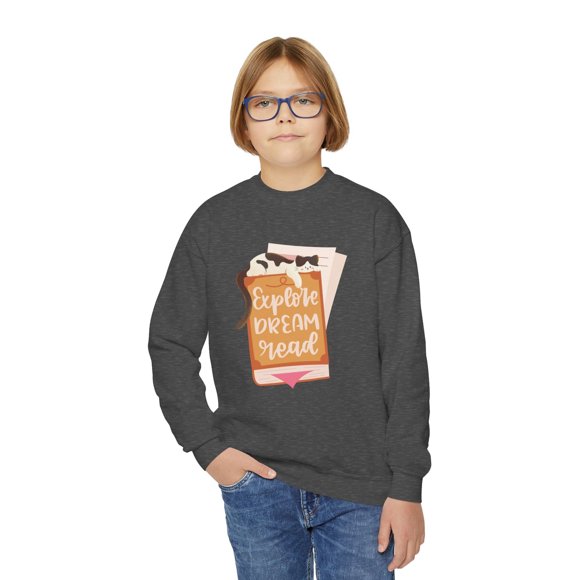 Boy wearing a dark gray sweatshirt with a graphic design of a cat sleeping on a book and text 'Explore. Dream. Read.'