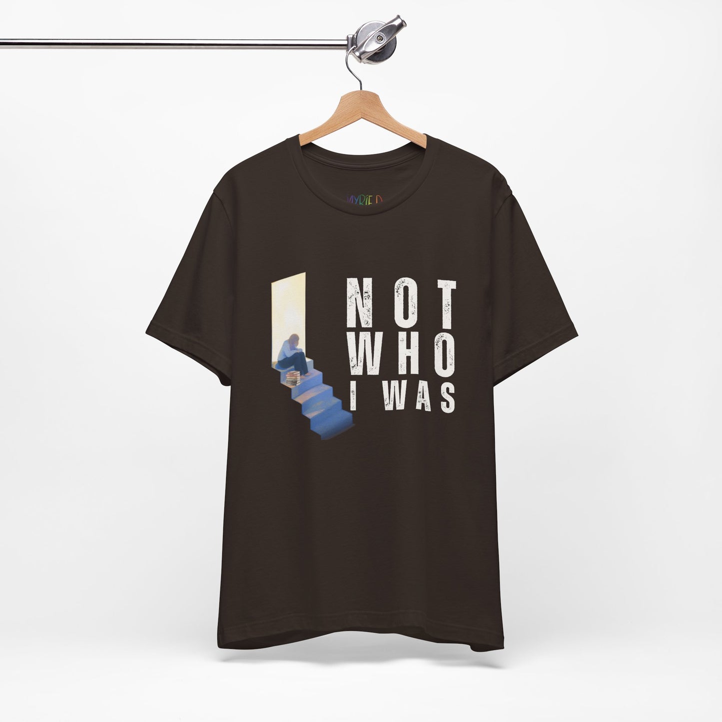 Brown t-shirt with person sitting at the top of the stairs, lit from behind and text 'Not Who I Was'